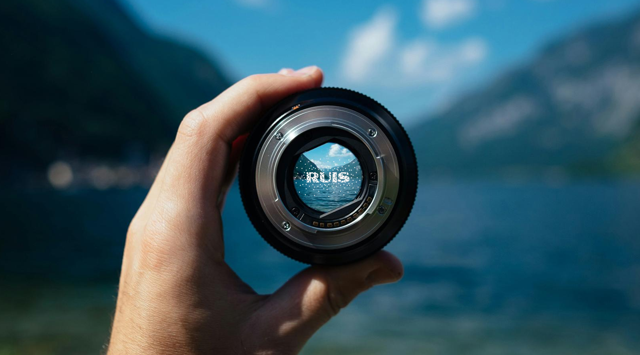 Een hand houdt een cameralens vast met het RUIS-logo scherp in beeld.